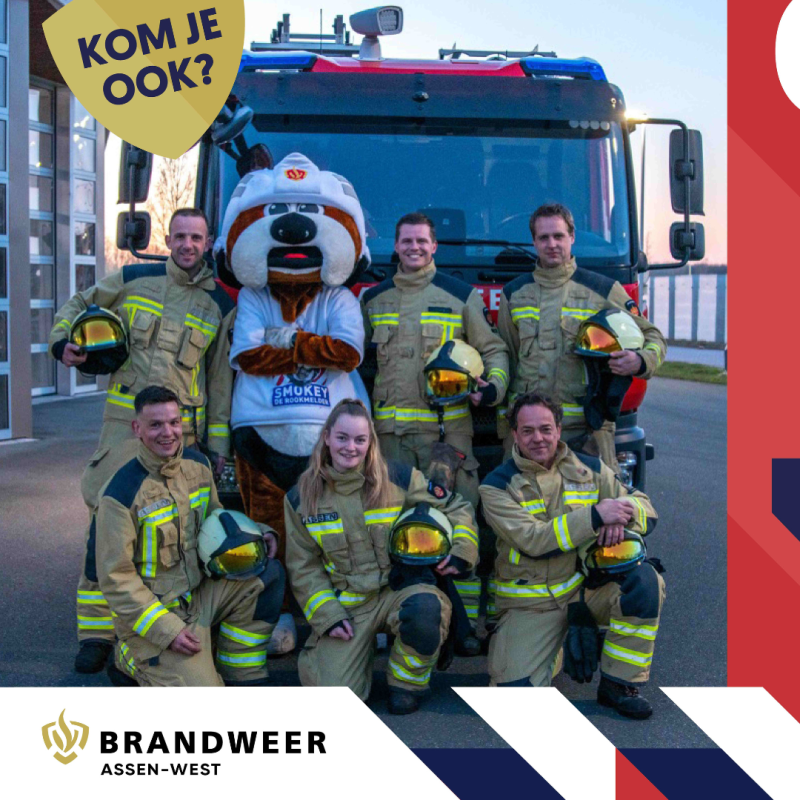 Op de achtergrond staat een brandweerwagen. Voor de brandweerwagen staan 6 brandweerlieden geposeerd met de mascotte. De mascotte is een persoon in een hondenpak, die smokey heet. De brandweerlieden hebben hun brandweerpak aan, houden een helm vast en lachen.